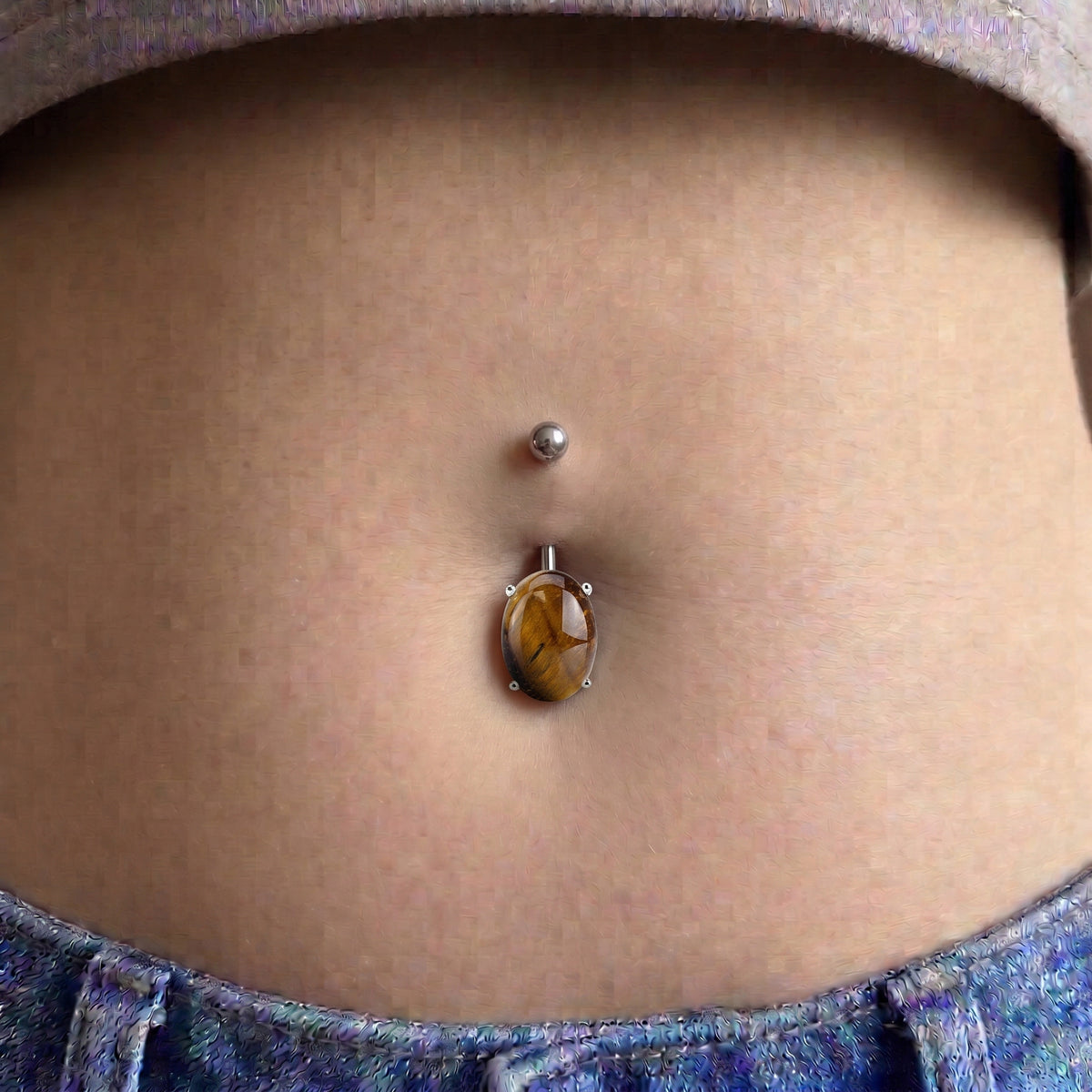 Natural tigers eye oval gemstone pictured in the belly button piercing of a female model.