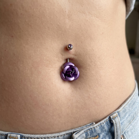 A purple rose belly button ring in the belly button piercing of a female model.
