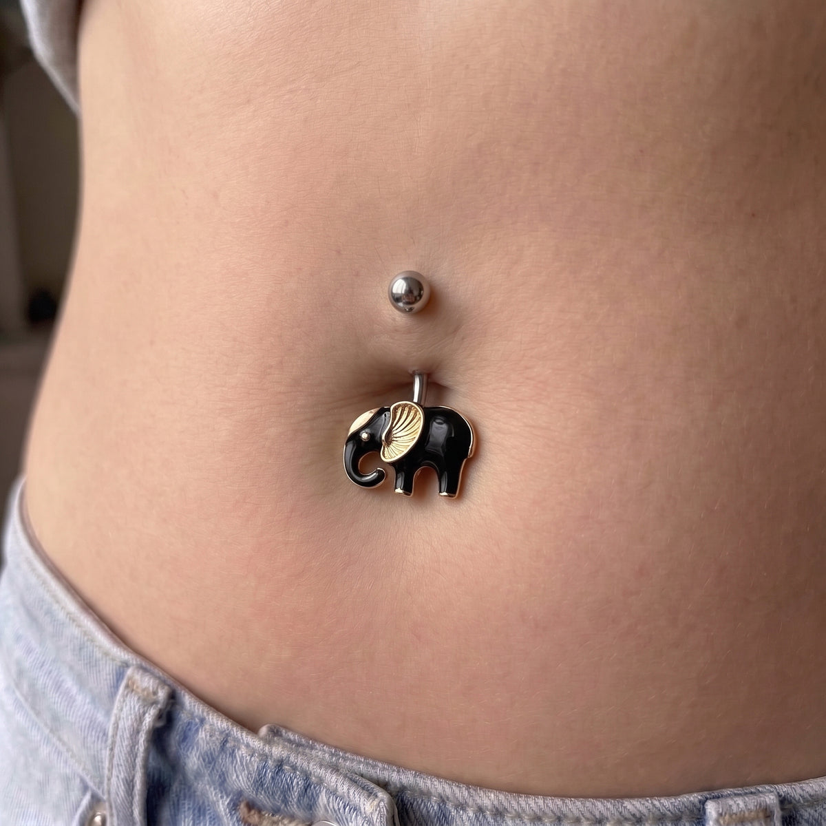 A black and gold elephant belly button ring in the belly piercing of a female model.