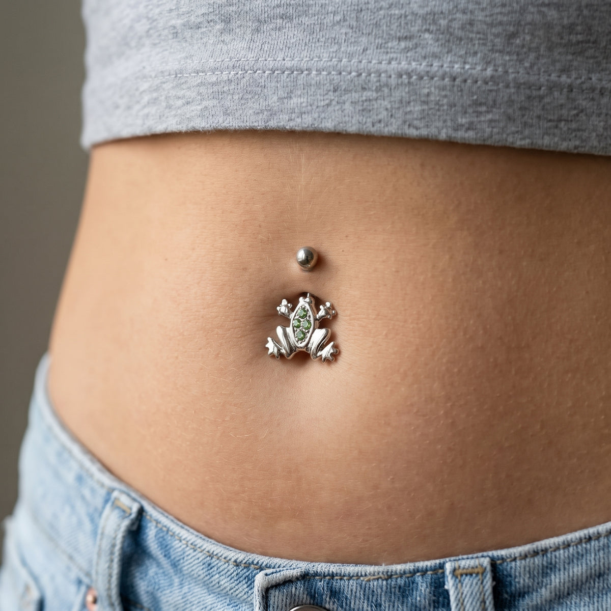 A frog belly button ring in the piercing of a female model.