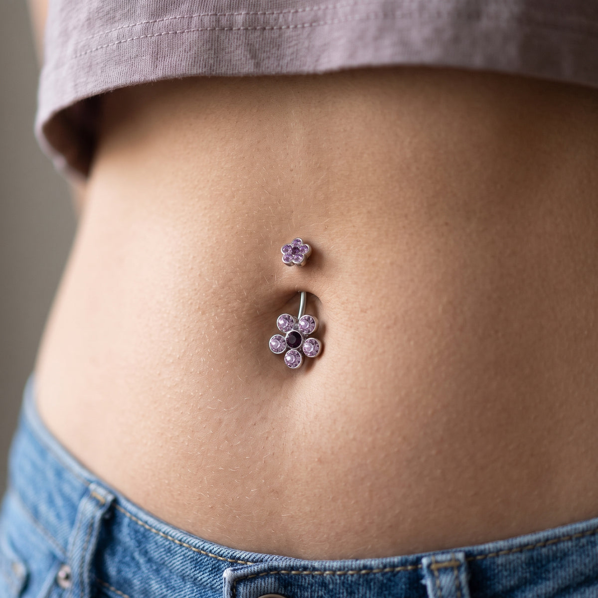 A purple petal flower belly button ring in the piercing of a female model.