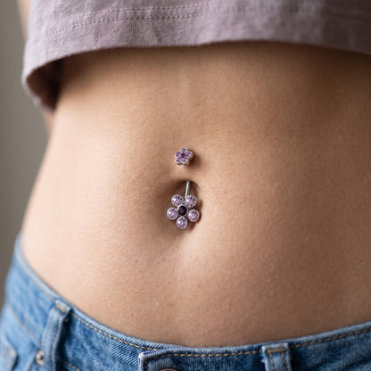 A purple petal flower belly button ring in the piercing of a female model.