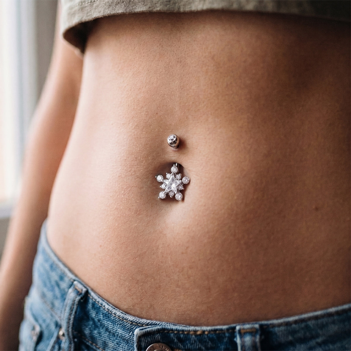 A star design cubic zirconia crystal belly button ring in the belly piercing of a female model.